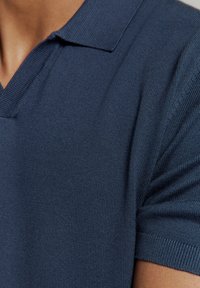 Navyblauwe polo met een V-hals ontwerp, geribde kraag en korte mouwen, gemaakt van een textuur gebreide stof.