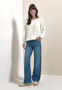 Hvid langærmet top med rund hals, parret med blå vide jeans og lyse, strukturerede sneakers. Enkel design, afslappet stil.