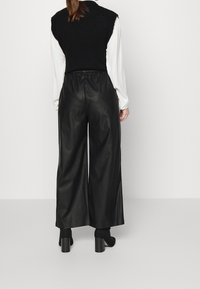 Pantalones anchos de talle alto en color negro, hechos de un material brillante similar al cuero. La cinturilla es elástica para mayor comodidad.