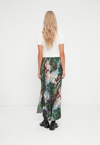 Gonna maxi in tessuto leggero, con una stampa di natura colorata che presenta alberi e case, spacco alto e una consistenza liscia. Indossata con tacchi a blocco neri.