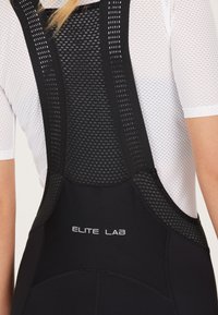 Zwarte sportieve bibshorts met gaasbandjes, logo "ELITE LAB," aansluitend ontwerp en textielstof voor ademend vermogen.