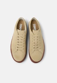 Beiga mockasinsneakers med rund tå, sex öglor och en brun gummisula. "Camper"-logotyp synlig inuti. Slät yta.