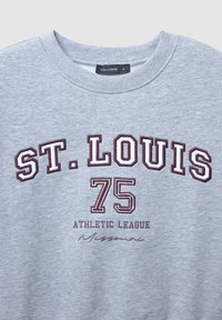 Felpa grigia con scollo rotondo presenta la scritta "ST. LOUIS 75 ATHLETIC LEAGUE" in testo bordeaux e "Missouri" in corsivo sottostante. Materiale in cotone.