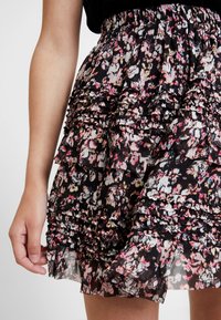 Musta kukkakuvioinen hame, jossa on kerroksittainen röyhelösuunnittelu ja vaaleanpunaisia, valkoisia ja vihreitä kuvioita. Venyvä vyötärönauha, kangas vaikuttaa kevyeltä ja läpikuultavalta.