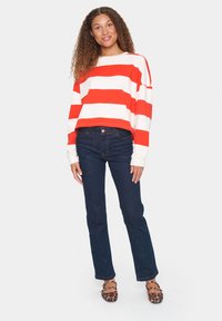 Felpa corta a righe rosse e bianche, jeans blu e ballerine con stampa animale. Maniche lunghe, vestibilità rilassata e denim scuro con cuciture chiare.