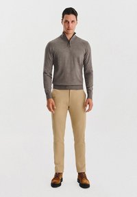 Szary sweter z zamkiem szyjnym, beżowe dopasowane spodnie i brązowe buty na sznurowadłach. Gładka tekstura, casualowy design, z nowoczesnym krojem.