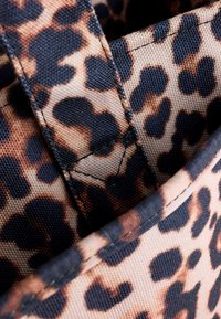 Materiał w leopardzie cętki z mieszanką jasnobeżowych i ciemnobrązowych plam, charakteryzujący się teksturowanym materiałem i widocznymi szwami wokół krawędzi.