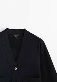 Navy knitted cardigan featuring a V-neck, single button closure, two front pockets, and ribbed detailing at the neckline and hem.