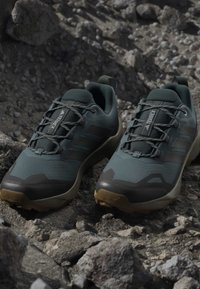 Buty trailowe z ciemnozieloną tekstylną cholewką, gumowymi akcentami i solidną podeszwą dla lepszej przyczepności na skalistym terenie. Lekka i przewiewna konstrukcja.