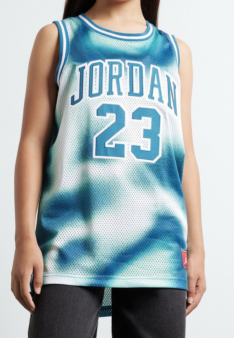 Persona que lleva una camiseta de baloncesto sin mangas con diseño tie-dye en azul y blanco, con "Jordan" y el número "23" en grandes letras y números azules.