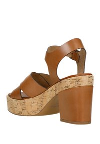 Sandali platform in pelle marrone con dettagli in sughero, caratterizzati da cinturini larghi e un tacco spesso. Texture liscia con una leggera lucentezza.
