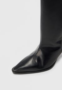 Bottes basses en cuir noir avec une pointe arrondie, une texture lisse et un design épuré et minimaliste sans éléments visibles ni ornementations.