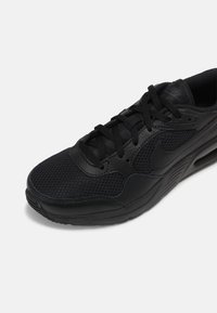 Baskets de sport noires avec une tige en mesh respirant, des accents en cuir lisse, un bout arrondi et une semelle en caoutchouc épaisse avec une texture antidérapante.