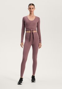Long-sleeve wrap top and high-waisted leggings in a soft mauve color, made from stretch fabric. Features a fitted design with a tied waist.