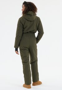 Combinaison rembourrée verte avec capuche, taille élastique et manches longues. Jambes à la cheville et coupe décontractée. Tissu à texture douce.