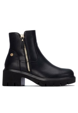 Schwarzer Leder-Stiefelette mit klobigem Absatz, seitlichem Reißverschluss und kleinem rundem goldfarbenem Emblem nahe der Ferse auf weißem Hintergrund.