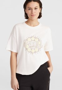 Vit bomulls-t-shirt med oversized passform, med rundad nederkant och en central grafisk logotyp i beige och gult. Matchas med svarta byxor.
