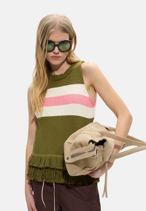 Kobieta w dużych okrągłych okularach przeciwsłonecznych i oliwkowozielonym dzianinowym topie bez rękawów z różowymi i białymi paskami, trzymająca beżową torebkę.