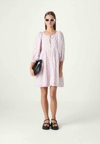 Pink floral mini kjole med puffærmer, nøglehul halsdetalje og flagrende skør. Tilbehør inkluderer en sort taske og solbriller. Sorte platform sko.