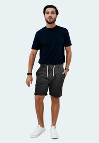 Marineblaues T-Shirt mit kurzen Ärmeln, schiefergraue Shorts mit Kordelzug und umgeschlagenen Säumen, kombiniert mit weißen Turnschuhen. Lässiges Outfit an einem Modell.