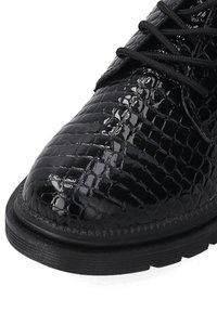 Czarne lakierowane buty ze skóry z fakturą w wzór krokodylej skóry. Posiadają czarne sznurówki oraz gumową podeszwę z rowkami zapewniającymi przyczepność.