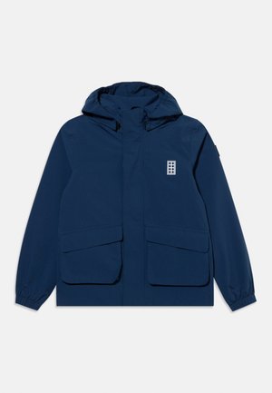 Veste à capuche bleu marine avec fermeture éclair frontale, deux grandes poches à rabat, poignets élastiques et un petit logo rectangulaire sur la poitrine.