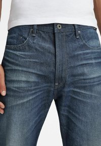 Dark blue denim jeans with a smooth texture, featuring front pockets, a zipper fly, and subtle fading along the legs.