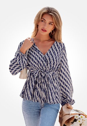 Bluzka w granatowo-kremowy wzór z dekoltem w serek, długimi bufkowymi rękawami i wiązaniem w talii. Połączona z jasnoniebieskimi dżinsami i torebką.