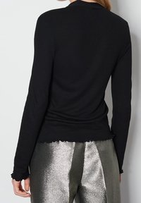 Svart långärmad topp med ribbad textur, med en åtsittande design och fransad nederkant, i kombination med metalliska silverbyxor.