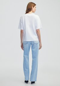 Witte katoenen t-shirt met een losse pasvorm, korte mouwen en een ronde hals. Gepaard met lichtblauwe denim jeans en zwarte hakken.