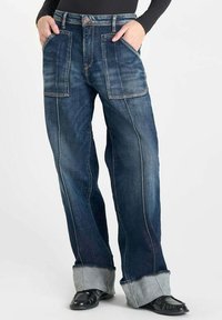 Jeans de mezclilla oscuros de pierna ancha con grandes bolsillos frontales, costuras en contraste y dobladillo con vuelta, con un diseño clásico de cinco bolsillos.