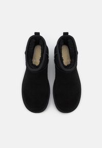 Botas de tobillo de ante negro con un suave forro de piel de pelo, punta redondeada y tirador en la parte trasera. Textura suave con un diseño minimalista.