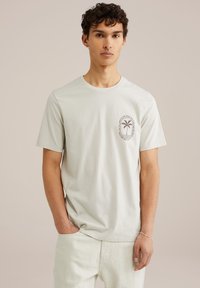 Lys grå bomulds t-shirt med korte ærmer og rund halsudskæring, der har et palmetræ grafisk billede i et cirkulært design på venstre bryst.