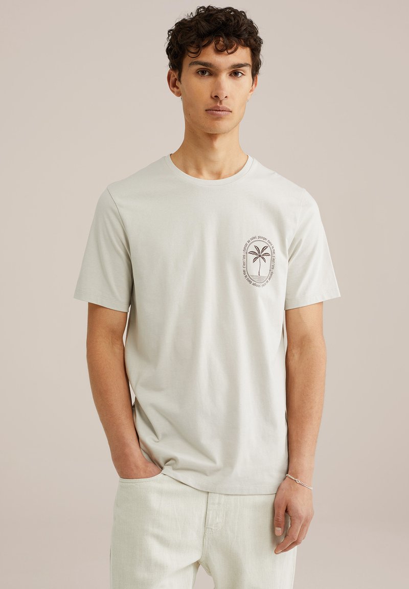 Lys grå bomulds t-shirt med korte ærmer og rund halsudskæring, der har et palmetræ grafisk billede i et cirkulært design på venstre bryst.