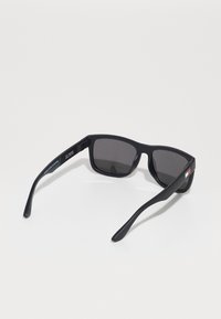 Gafas de sol negras rectangulares con lentes oscuros, acabado mate y varillas delgadas. Presentan un pequeño detalle de logo en una de las varillas.