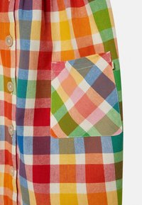 Kolorowa koszula w kratę z wzorami w kolorach czerwonym, niebieskim, zielonym, pomarańczowym i żółtym. Zawiera kieszonkę naszywaną po lewej stronie oraz zapięcie na guziki.