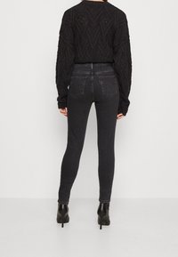 Suéter negro de punto con un patrón de chevron texturizado, combinado con jeans skinny negros de cintura alta y botas de tacón negro tobilleras.