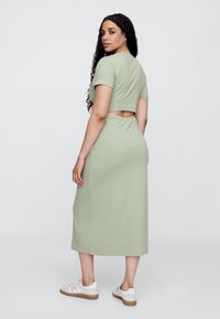 Miętowa sukienka dopasowana, z krótkim topem i wycięciem na plecach. Miękka w dotyku, o długości do kolan, w zestawieniu z białymi trampkami.