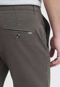 Pantaloni in cotone grigi con una tasca posteriore dotata di chiusura con bottone e un accento decorativo a righe. Il tessuto ha una superficie liscia.