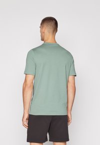 Mintgrünes T-Shirt mit kurzen Ärmeln und runder Ausschnitt, glatter Textur und lockerer Passform, kombiniert mit schwarzen Shorts.