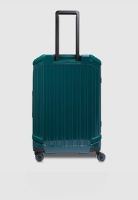 Tegelkleurige koffer met harde schaal en verticale ribbels, een zwarte uitschuifbare handgreep en vier wielen voor mobiliteit. Duurzaam materiaal met een glanzende afwerking.