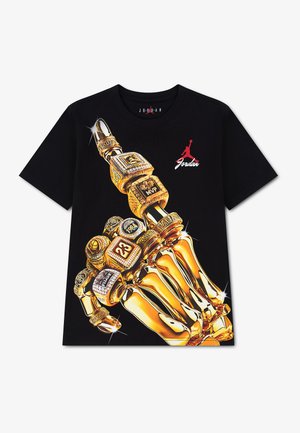 Schwarzes T-Shirt mit einer großen Grafik einer goldenen Skelett-Hand mit mehreren Meisterschaftsringen, rotem Jordan-Logo und Schriftzug in der Nähe des Kragens.