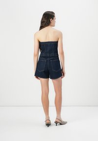 Salopette in denim con design senza spalline, colore blu scuro, vita elastica e pantaloni corti. Presenta tasche posteriori e una texture liscia.
