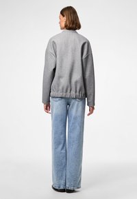 Szary, oversize'owy sweter o teksturowanym wykończeniu i prążkowanym dole, zestawiony z jasnoniebieskimi, szerokimi spodniami jeansowymi oraz czarnymi butami, widoczny od tyłu.