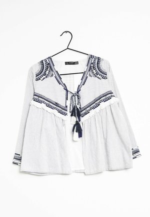 Blusa a strisce con scollatura a V, ricamo decorativo in blu navy, lacci con nappine e maniche a tre quarti. Realizzata in tessuto leggero.