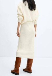 Ensemble en tricot côtelé crème comprenant un pull et une jupe midi. Présente une coupe ample et un tissu texturé. Associé à des bottes en cuir marron hautes.