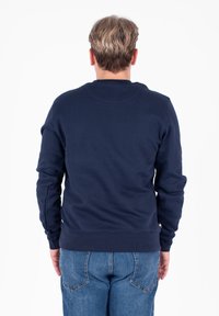 Granatowy sweatshirt z długimi rękawami, okrągłym dekoltem i prążkowanymi mankietami. Miękka tekstura, brak widocznych wzorów, zestawiony z dżinsowymi spodniami.