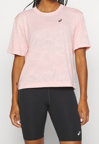 Light pink athletic t-shirt with a textured floral pattern, short sleeves, and a round neck; paired with black cycling shorts.