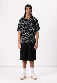 Maglietta nera a maniche corte con un motivo astratto bianco, abbinata a pantaloni cargo neri. Completato con calzini bianchi e sneaker color crema.