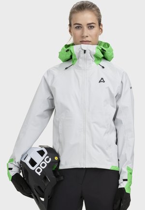 Wetterfeste weiße Jacke mit grünem Kapuzen- und Akzentdetails; verfügt über einen durchgehenden Reißverschluss und verstellbare Manschetten. Schwarzer Helm wird in der linken Hand gehalten.